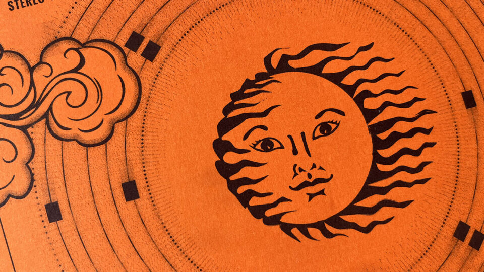 Nahaufnahme des orangefarbenen Risodruck-Covers mit stilisierter Sonne, geschwungenen Wolken und konzentrischen Kreisen. Die Druckstruktur ist deutlich sichtbar.